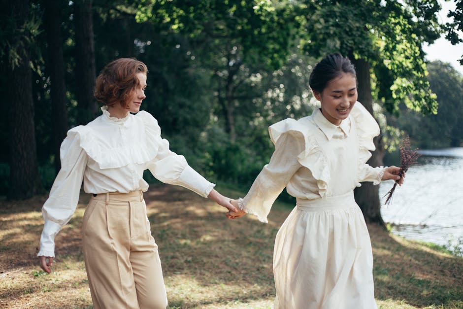 Two women holding hands and smiling while walking in a scenic park.