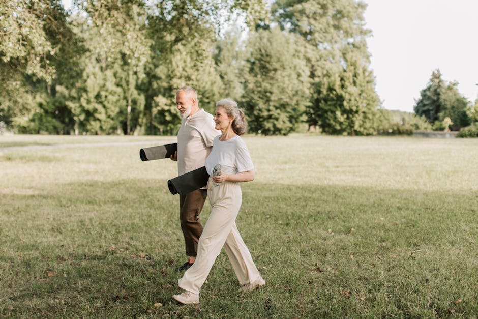 Elderly couple walking on grass carrying yoga mats, enjoying a sunny day outdoors.