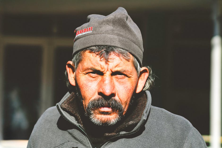 Close-up portrait of a mature man with a hat basking in sunlight outdoors.