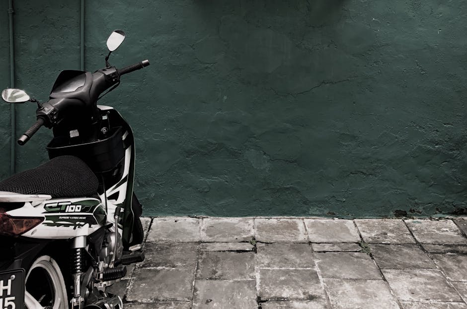 A motorcycle parked against a weathered green wall on a tiled pavement, urban setting.