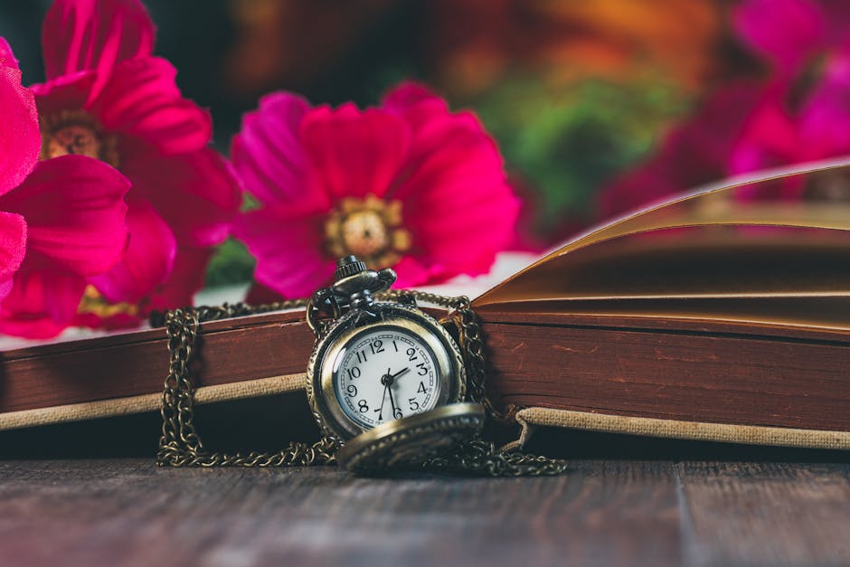 Close-up of a vintage pocket watch on a book, adorned with vivid pink flowers.