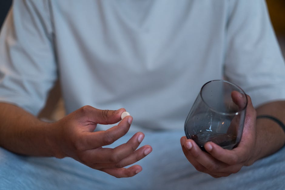 Close-up of an unrecognizable man taking a pill with a glass. Indoor setting.