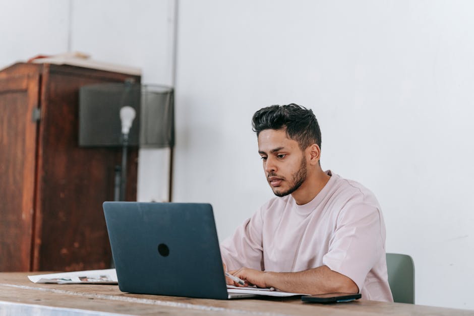 Focused young man working on a laptop in a minimalist home office setting.