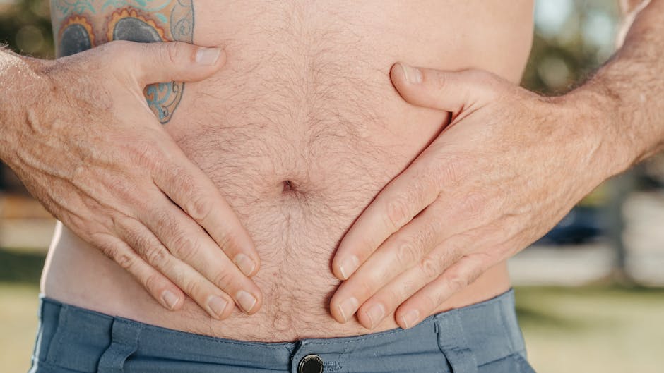 A close-up image of a man's stomach with tattoos, showcasing hands placed on either side, symbolizing health or discomfort.
