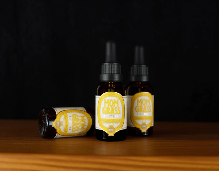 Close-up of Mom Grass CBD tincture bottles on a wooden surface with black background.