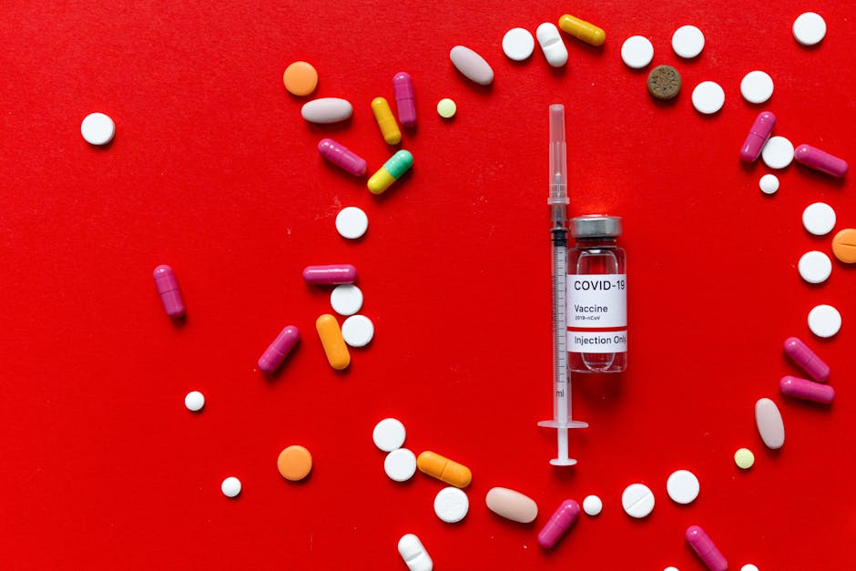 Close-up of COVID-19 vaccine vial with syringe and various pills on a red surface.