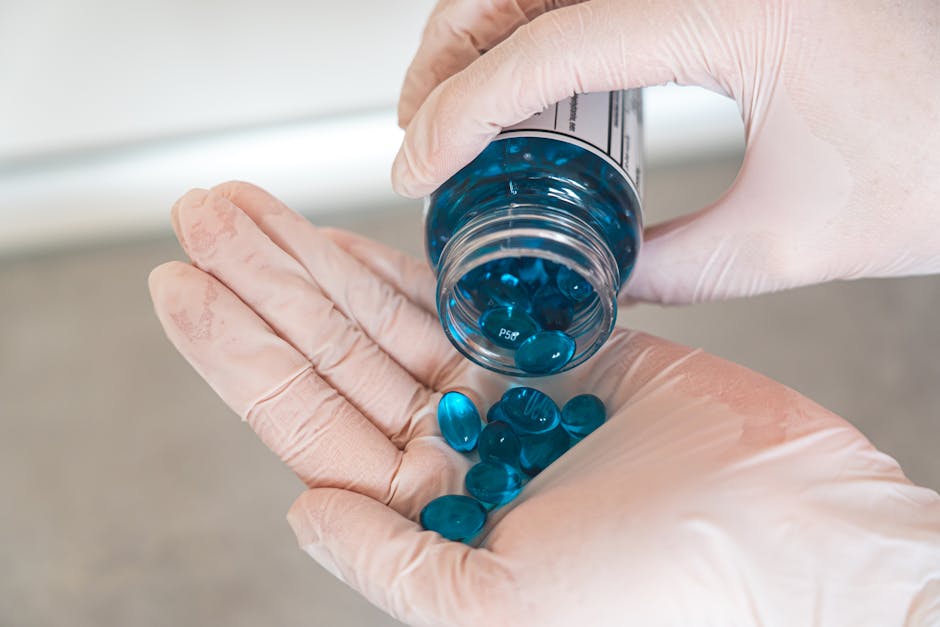 Close-up of a healthcare professional with latex gloves pouring blue capsules from a bottle.