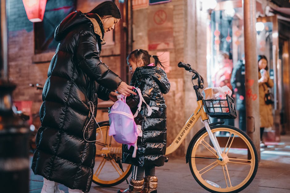 A mother helping her daughter with a backpack on a vibrant Beijing street at night.