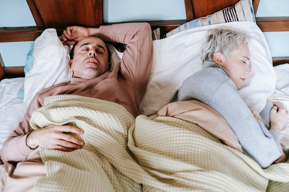 A middle-aged couple peacefully asleep in a cozy, well-lit bedroom setting.