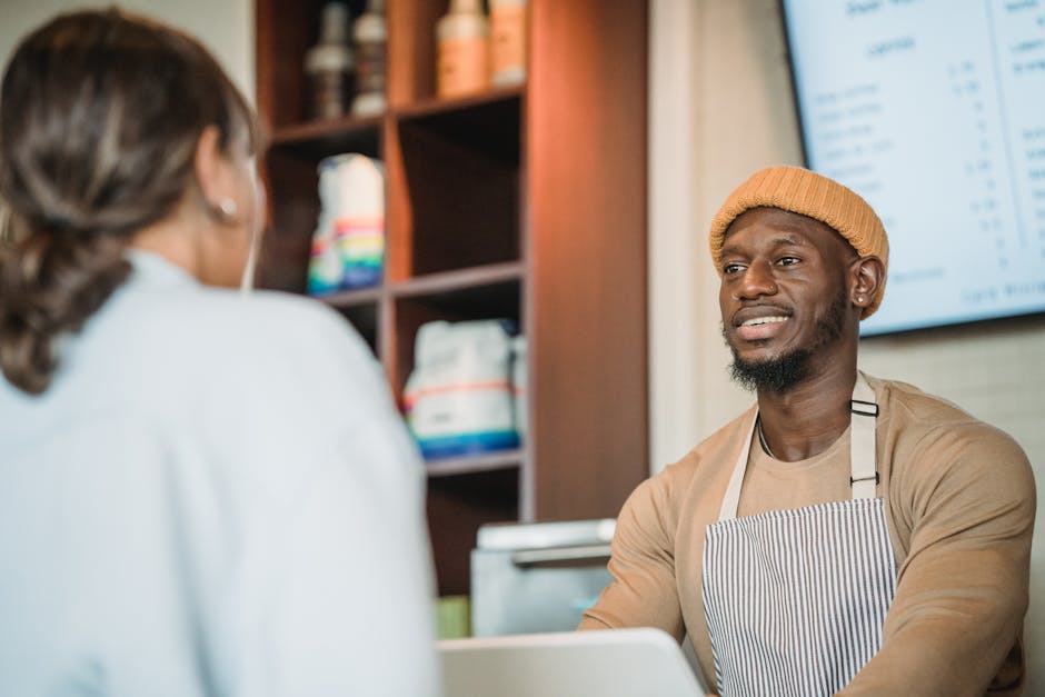 A smiling barista in an apron serves a customer at a cozy cafe counter.