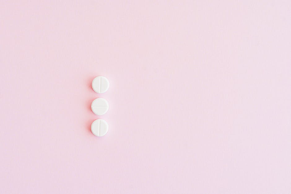 Three white pills arranged vertically on a pastel pink background for a minimalist medical concept.