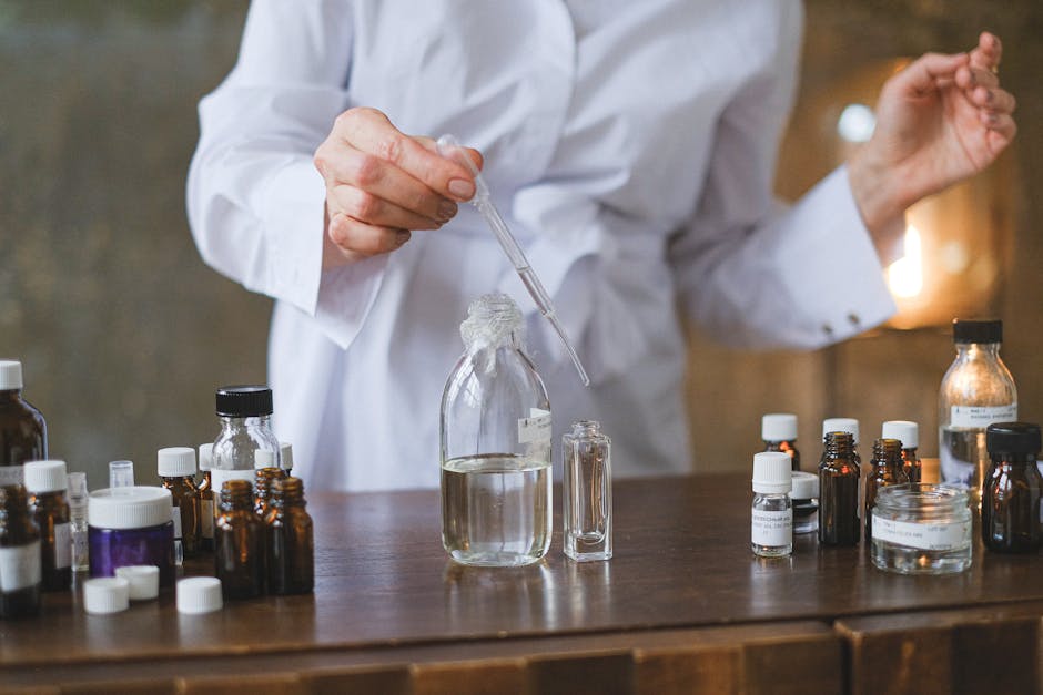 Person in lab coat using dropper to transfer liquid into clear glass bottles on a table.