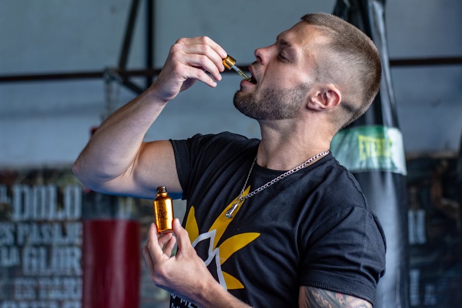 Adult man consuming hemp oil with a dropper in a gym. Emphasizes masculinity and wellness.