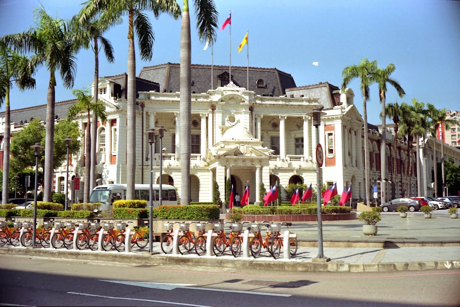 View of Taichung City Hall surrounded by palm trees and bicycles, under a clear blue sky.