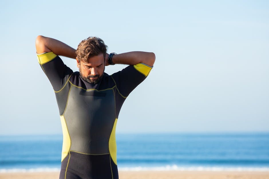 Bearded male in diving suit standing on sandy seaside and doing warm up exercise