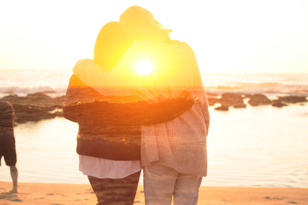 two people standing on a beach at sunset