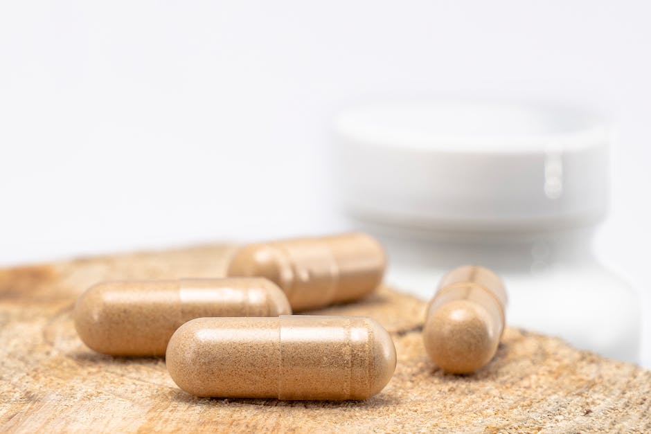 A close-up shot of brown capsules placed on a wooden surface with a blurred bottle in the background.