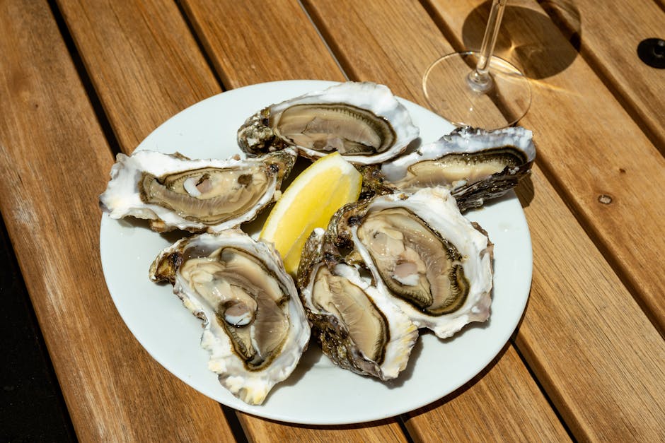 A plate of fresh oysters served with lemon wedge on a wooden table in daylight.
