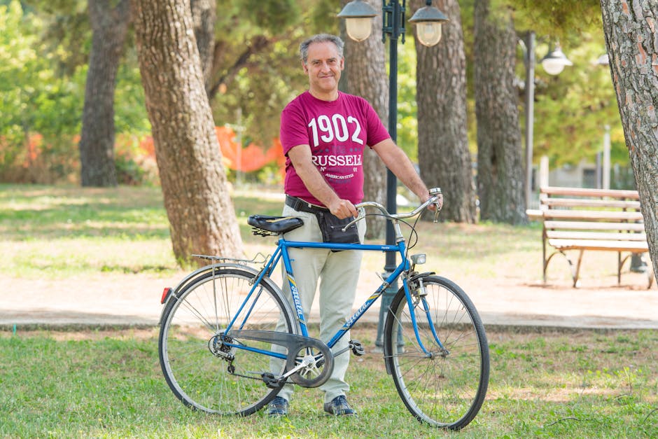 Middle-aged man smiling with a bicycle in a sunny park setting, showcasing leisure and happiness.