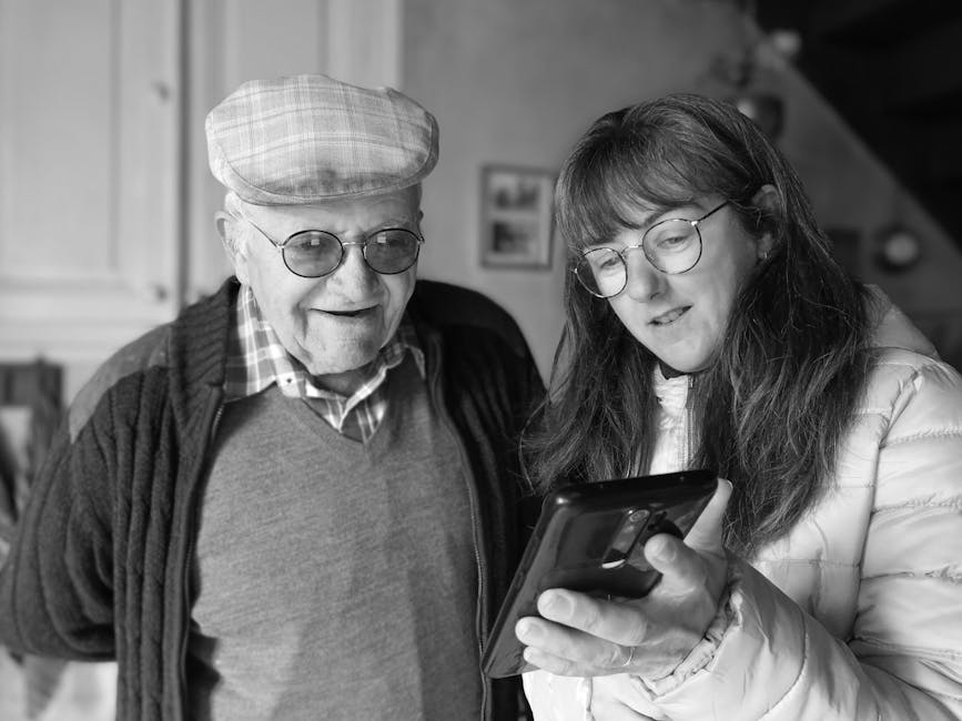 An elderly man and a woman together looking at a smartphone indoors, enjoying technology.