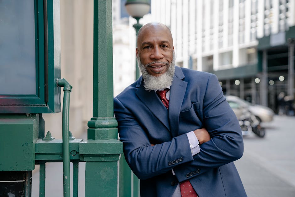 Smiling businessman in blue suit leaning against a railing in a city street.