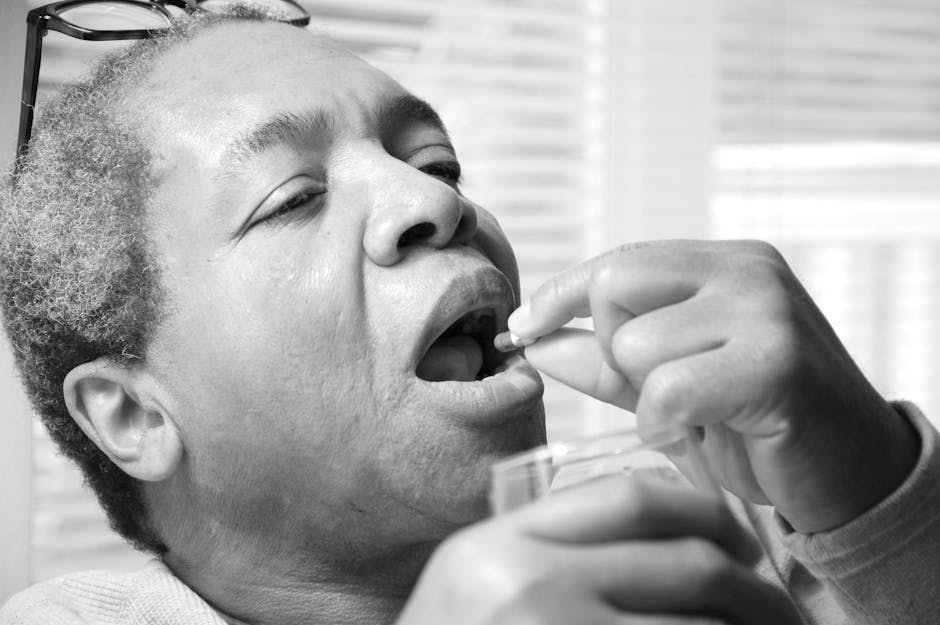 A senior man taking medicine with a glass of water indoors. Black and white photo.